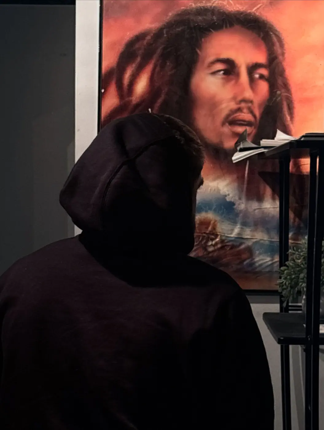 Michael Tennis Davis in a black hoodie, in front of a painted Bob Marley poster